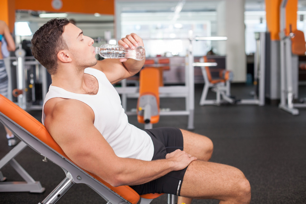 Cheerful young male sportsman is very thirsty