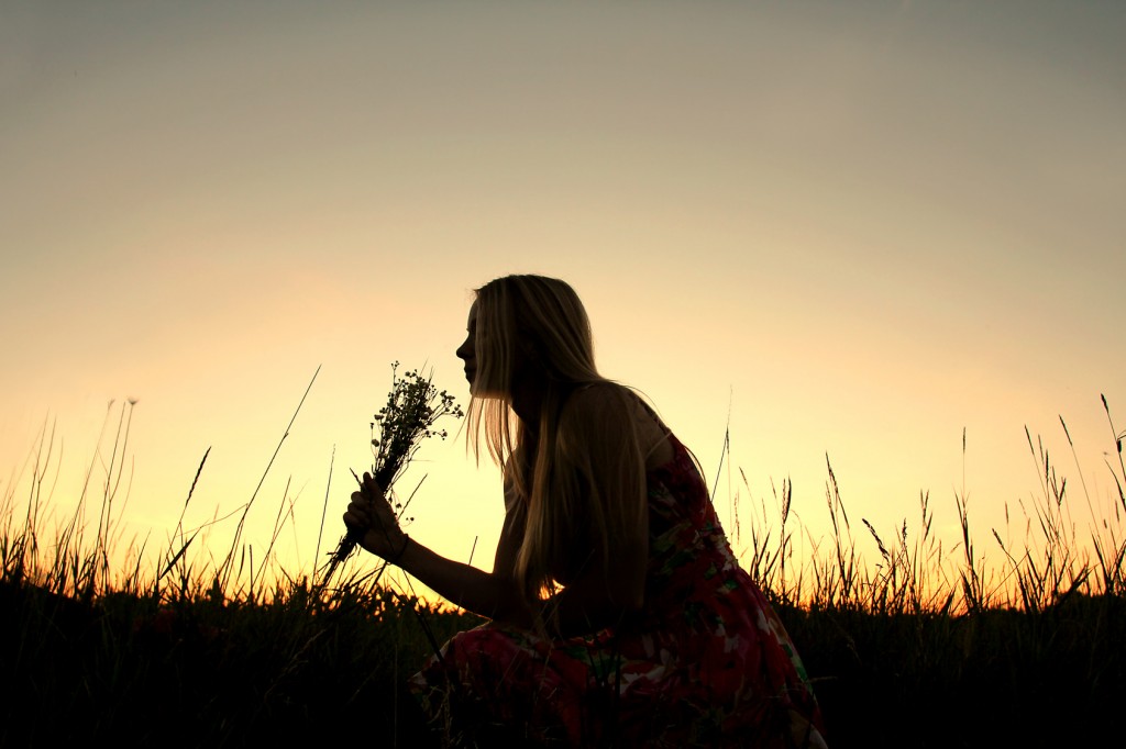 Silhouette of Girl Picking Flowers in Meadow at Sunset