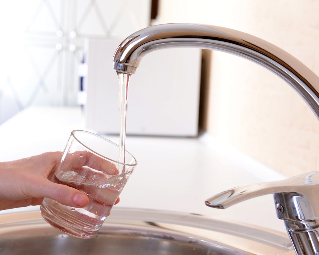 Hand holding glass of water poured from kitchen faucet