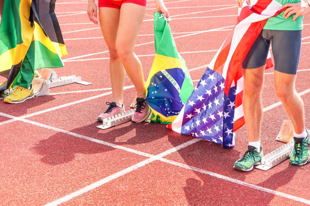 International sport athletes at stadium track holding national flags - Runners legs and feet at start grid cropped view from above - Professionals sportsmen celebrating victory of the competition