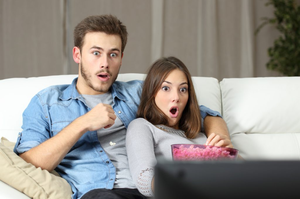 Amazed couple watching tv at home