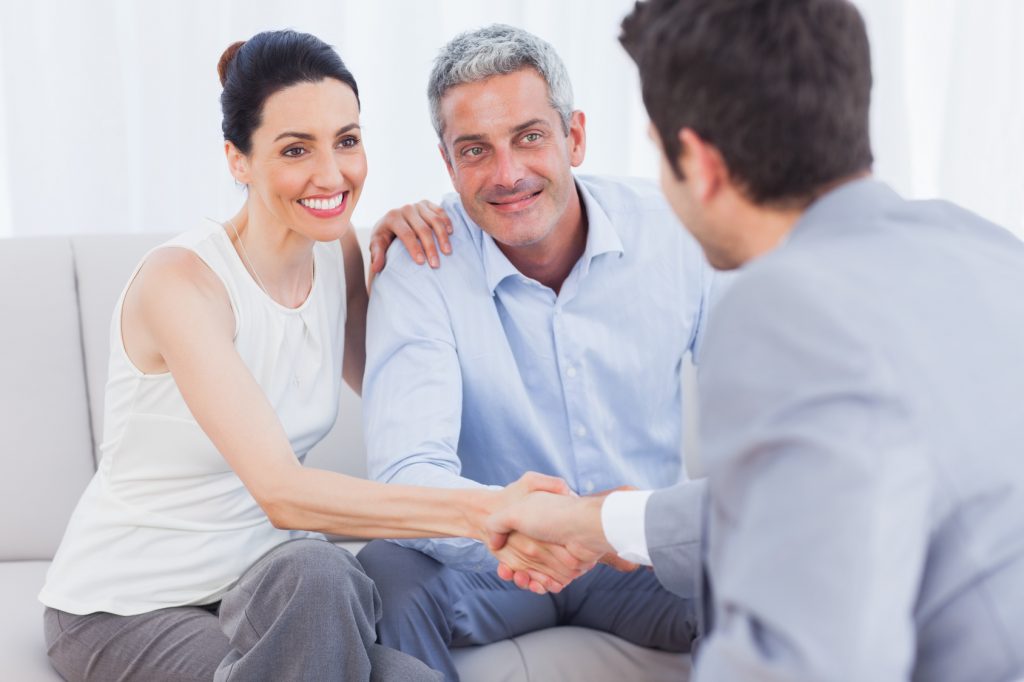 Woman shaking hands with salesman sitting beside husband on couch at home