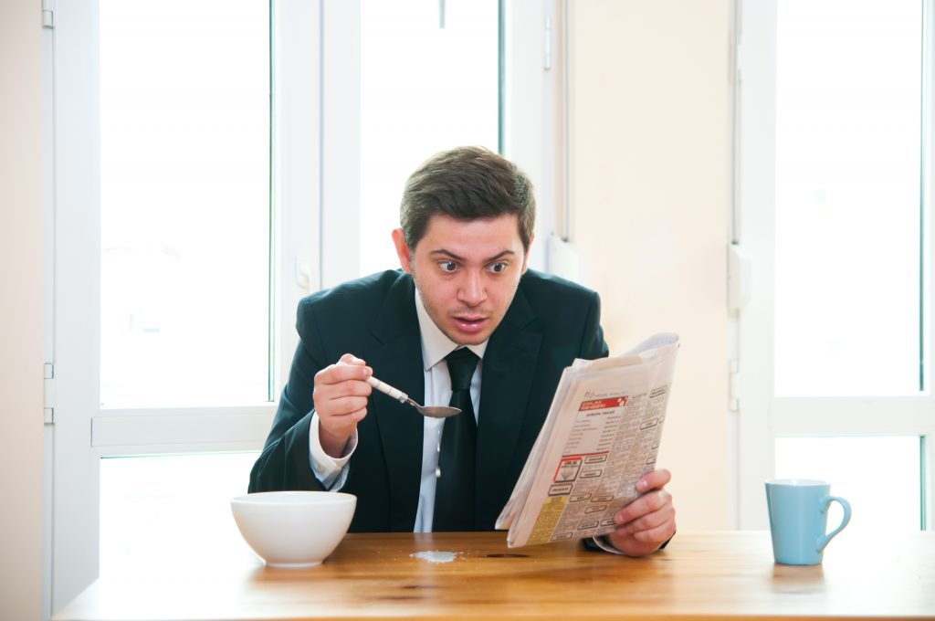 Young businessman having breakfast and reading newspaper