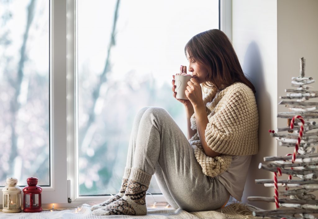 Young beautiful woman drinking hot coffee sitting on window sill