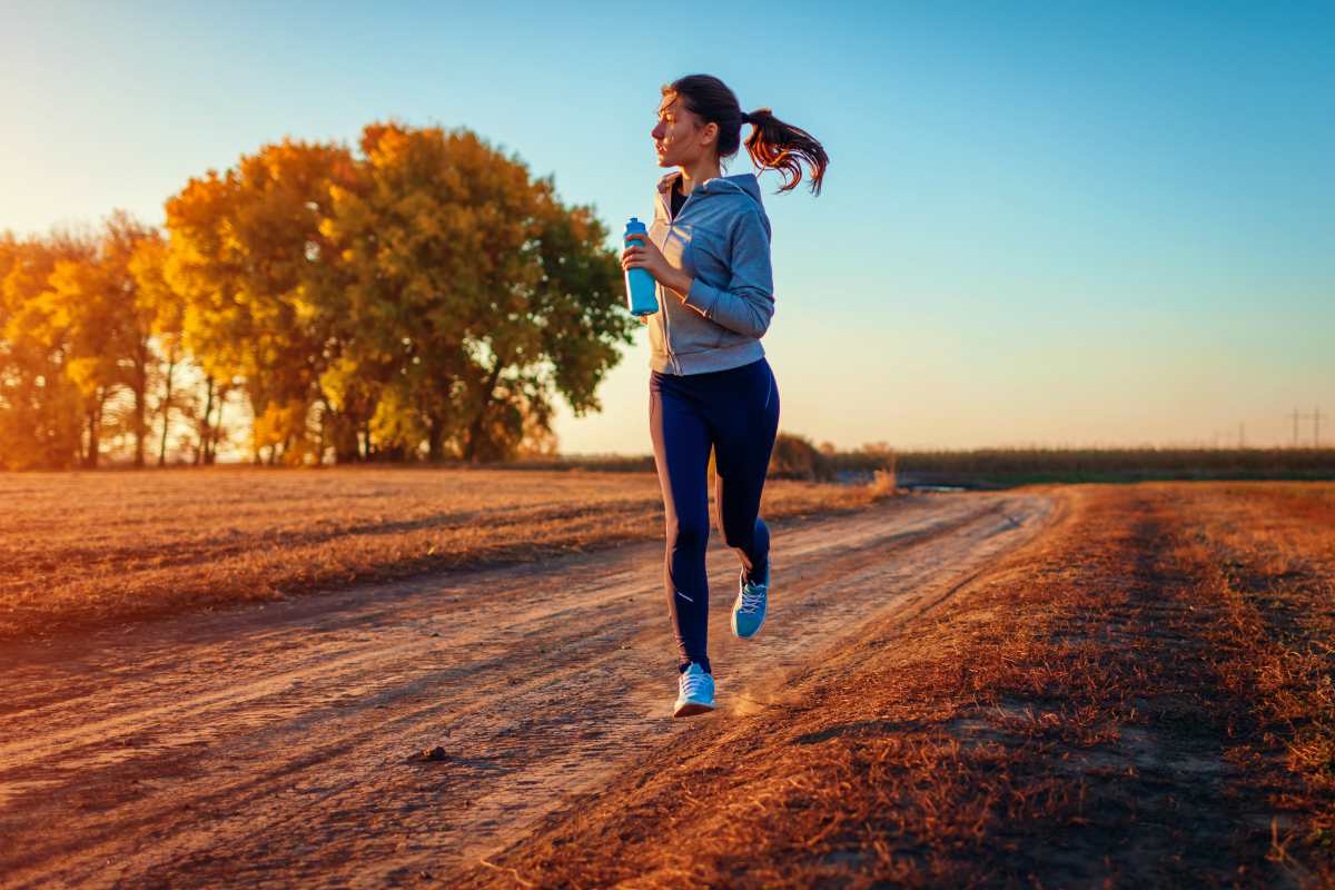 Woman running holding bottle of water in autumn field at sunset | Best Quick Workouts For Busy People Who Don't Have Much Time