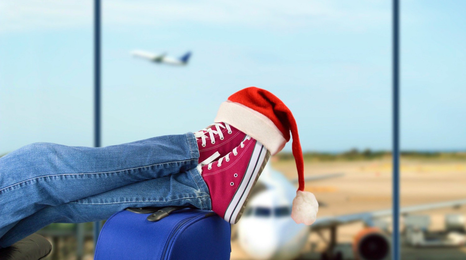 Young boy with his legs over the suitcase waiting at the airport | Travel Essentials For A Healthy Holiday