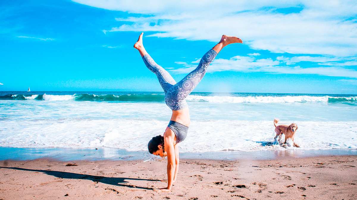 Woman performing inverted stand beside seashore | Benefits Of Drinking Water