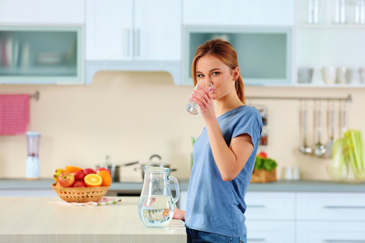 Young woman drinking water from glass in the kitchen | Alkaline Water Detox: How To Do It