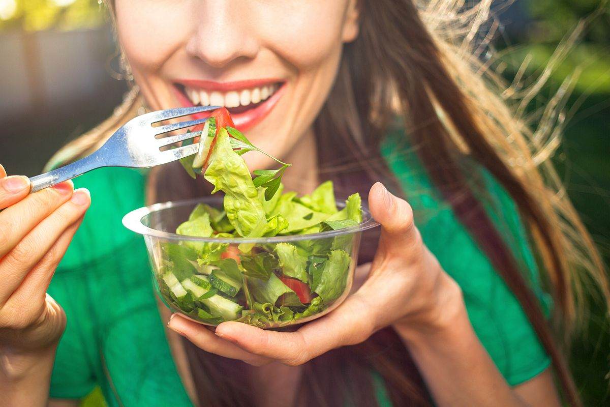 Smiling beautiful woman eating vegetable salad | What You Need To Know About The Alkaline Diet