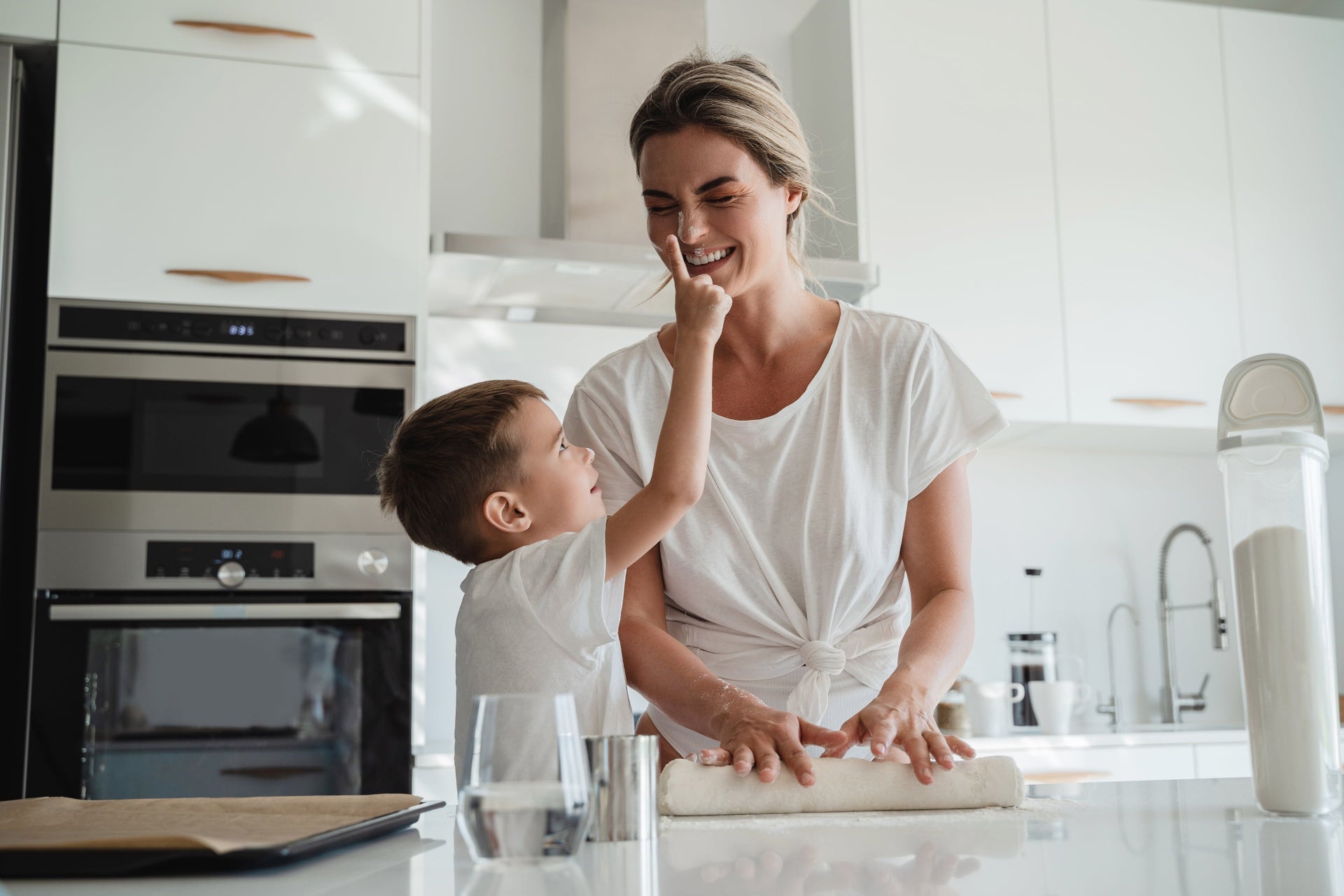 Woman and child in a modern kitchen, with the child playfully touching the woman's nose, and a glass of water on the counter top.