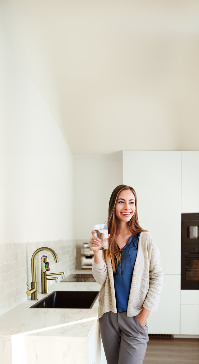 Woman holding a glass of  water in a modern kitchen next to Tyent UCE water ionizer